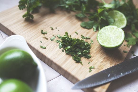 Cilantro and lime being chopped on a wooden chopping board in kitchen