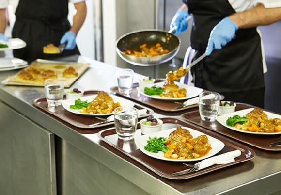 A szakács a serpenyőből a tálcán lévő tányérokra helyezi az ételt