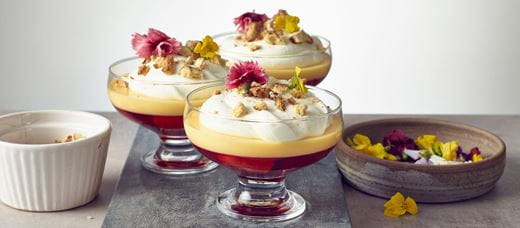 Trzy takie same żółto-czerwone desery z bitą śmietaną podane w pucharkach