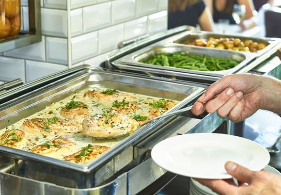 Osba nakładająca jedzenie z bemara w restauracji