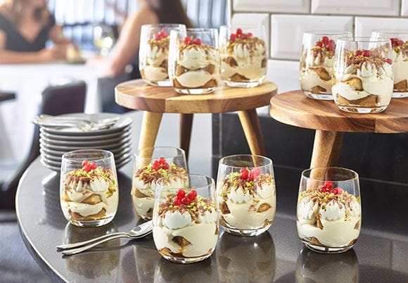 Porcje Panna Cotty podane w szklankach na blacie stołu restauracyjnego