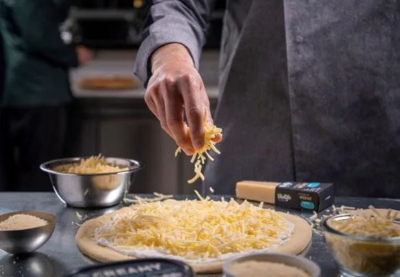 Pizza posypywana alternatywą sera Violife przez kucharza