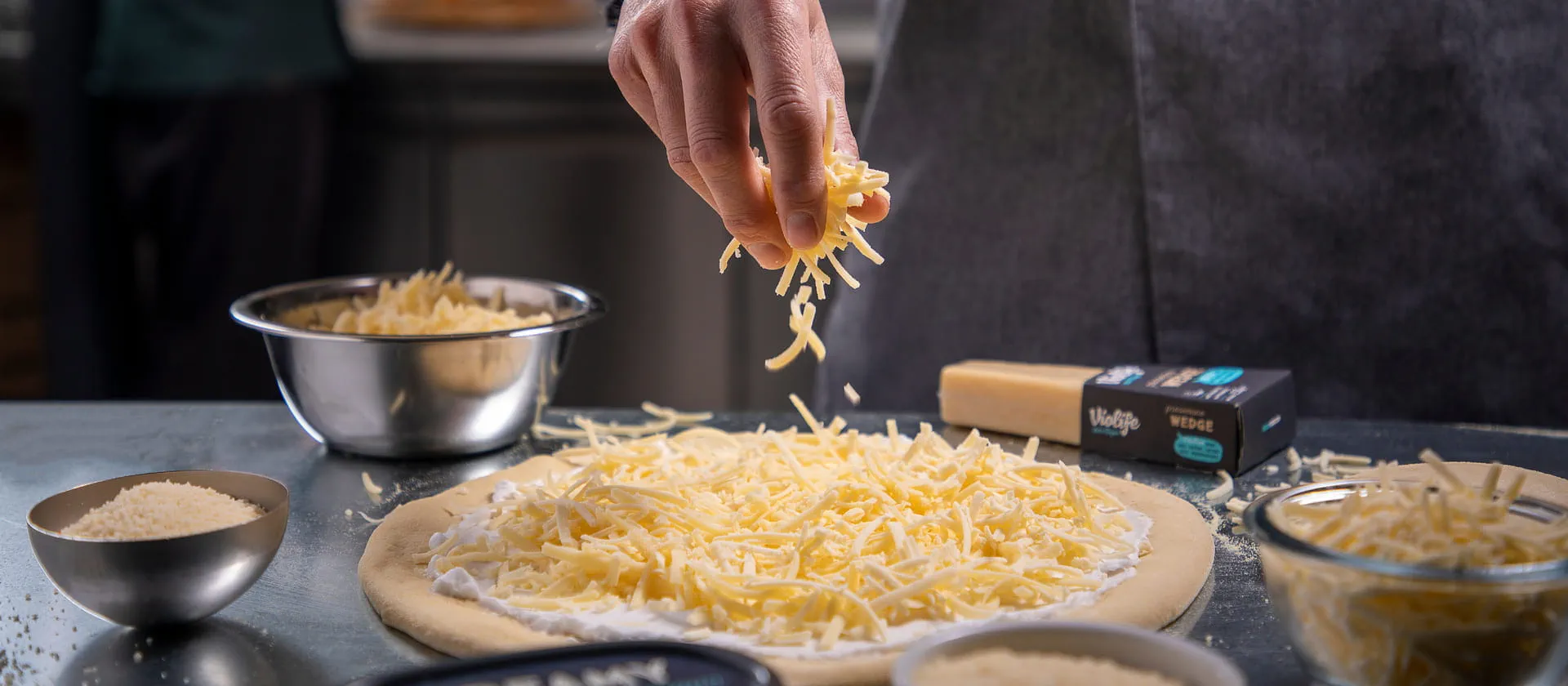 Kucharz posypujący pizze alternatywą sera Violife