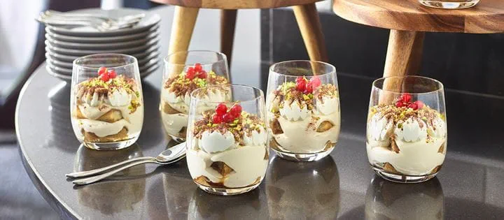 Porcje Panna Cotty podane w szklankach na blacie stołu restauracyjnego