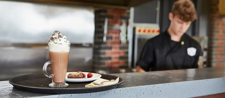 Kawa latte stojąca na blacie kawiarnianego baru. W tle pracujący kelner