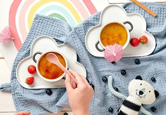 Dwie kawy podane na błękitnym kocu. Przy kawach pluszowy kot. W tle narysowana tęcza